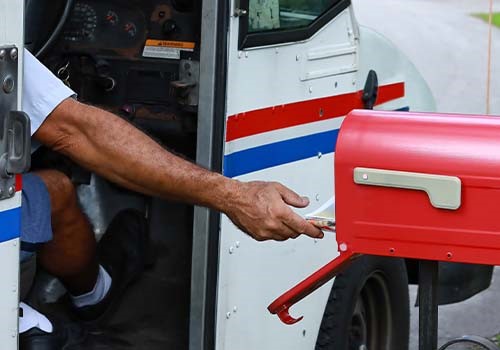 A mail carrier reaching out of his delivery truck to deliver mail.